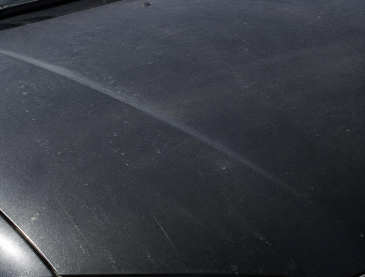 Dull, swirl-marked dark grey car hood before paint correction